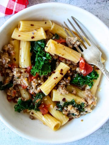 Sausage and kale pasta in a white bowl with a silver fork.